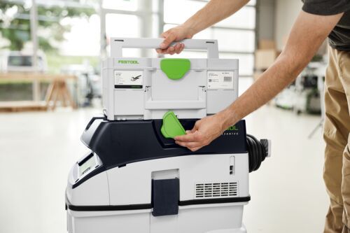 Person holding a FESTOOL tool chest in a workshop setting