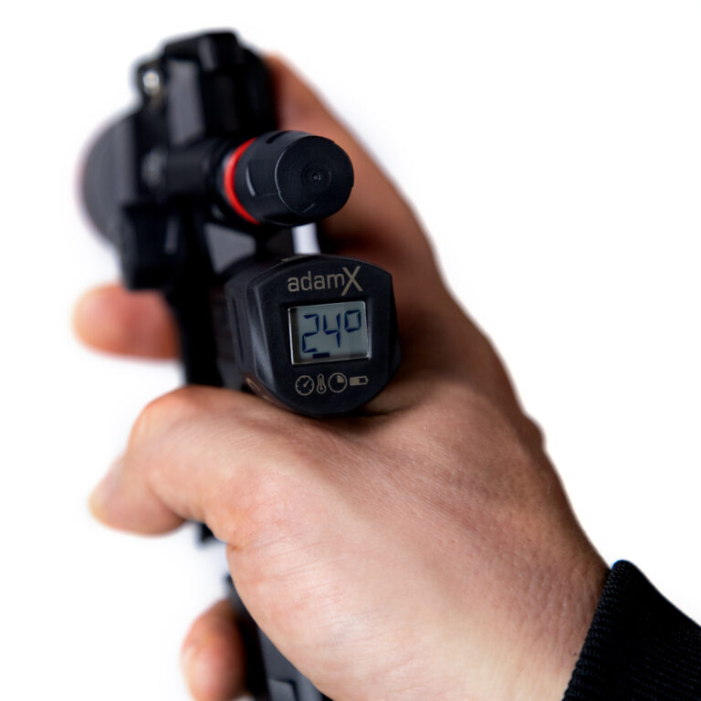 Hand holding a digital tire pressure gauge with 'adamX' branding.